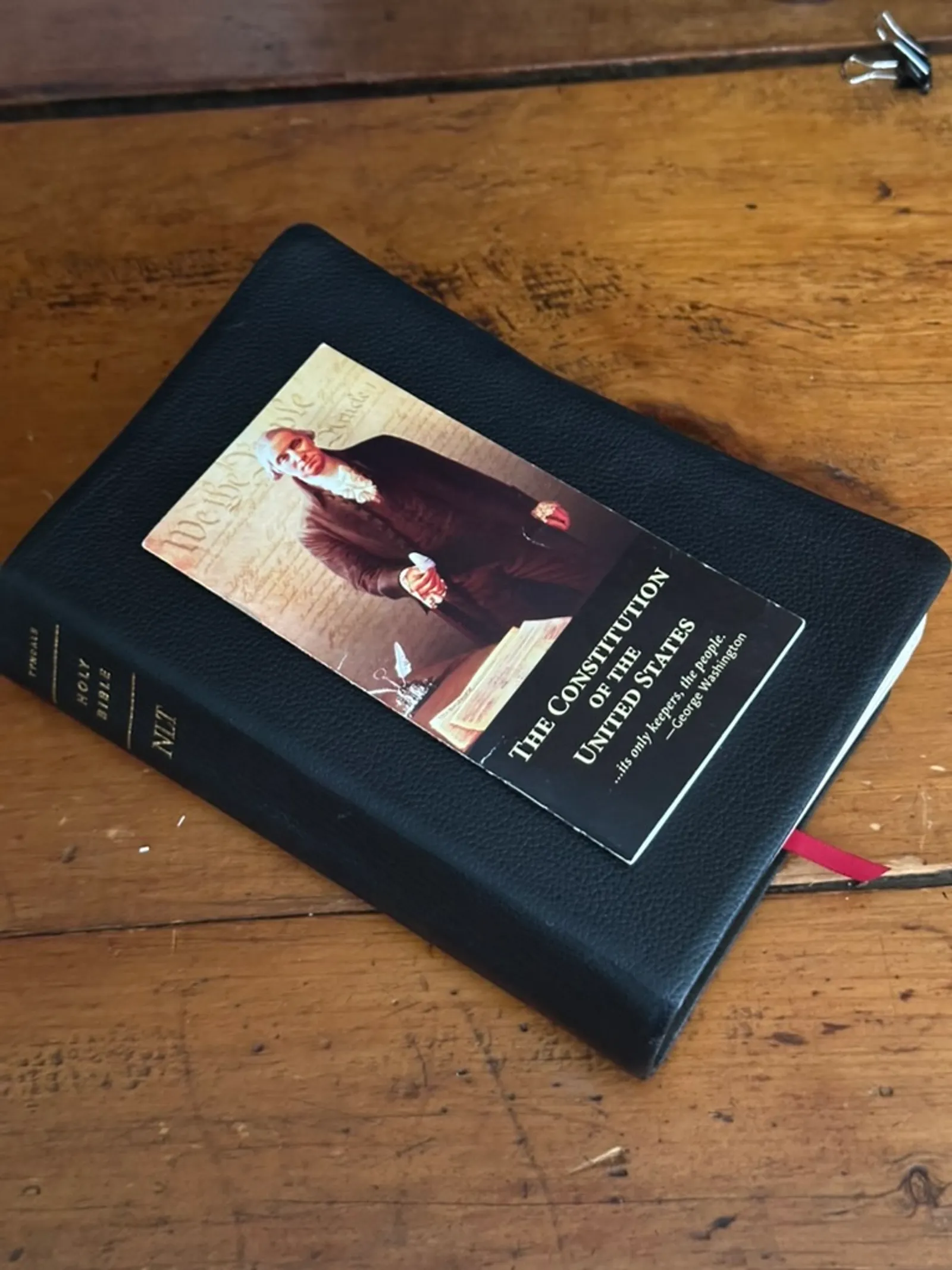 A black leather Bible on a wooden desk with a bookmark of the Constitution of the United States resting on top.